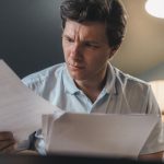 Homem analisa documentos financeiros sentado em um escritório rural.
