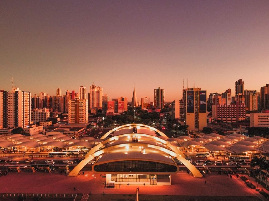 Vista aérea de Maringá ao entardecer, com o terminal intermodal e a área urbana da cidade.